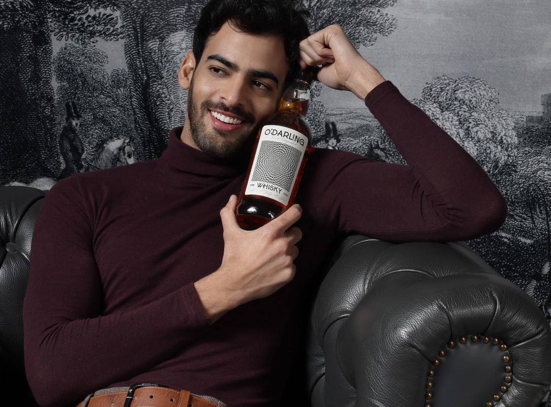 Image of a man sitting on the couch and smiling with a bottle of O'Darling Whisky